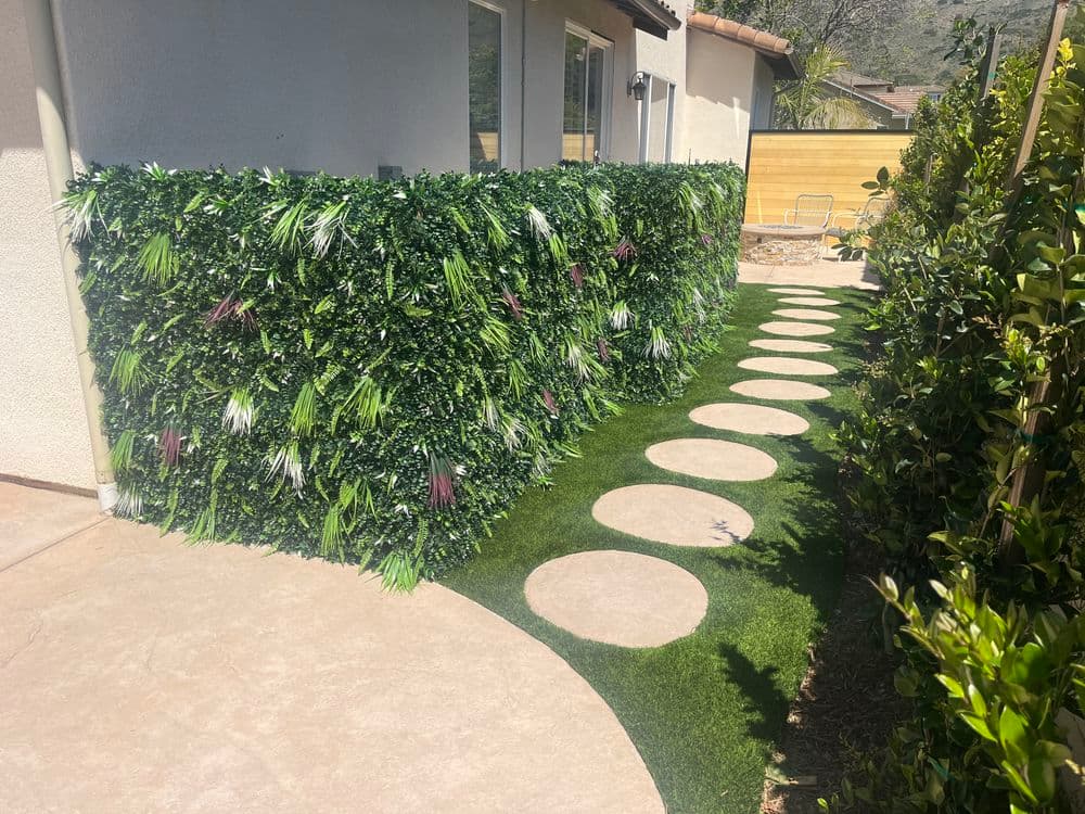 Artificial hedge privacy wall with stone pathway and green lawn in a residential garden.
